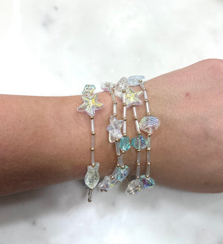 Bring all the beachy vibes to your summer outfits with this dreamy 5-piece bracelet stack featuring iridescent starfish, shell, and ocean-inspired beads in soft clear and aqua tones. Lightweight and easy to wear, these stretch bracelets can be worn stacked together for the perfect coastal statement or mixed and matched with your favorite everyday jewelry. The shimmer finish catches the light beautifully for the ultimate mermaid-inspired look.

DETAILS:
• 5-piece stretch bracelet set
