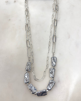 Sleek shine meets modern texture with this statement layered necklace. Featuring mixed silver-tone chains paired with organically shaped ripple beads, this piece brings effortless edge and polished style to any look. Lightweight and easy to wear, it’s perfect styled on its own or layered with other favorites for added dimension and everyday versatility.