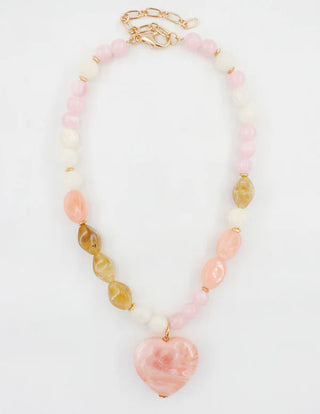 A soft mix of color and texture comes together in the Multi Stone Heart Pendant Necklace. Designed with an assortment of smooth pastel-toned beads and finished with a marbled heart-shaped pendant, this piece adds a romantic focal point with a playful, polished feel.

The balanced blend of pink, ivory, and warm neutral tones makes this necklace easy to style with everyday outfits or dressier looks. Wear it on its own as a statement or layer it with delicate chains for added dimension.